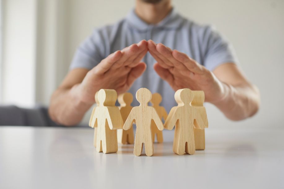 Persona con manos en forma de protección sobre unas figuras de madera que simulan un grupo de personas / trabajadores